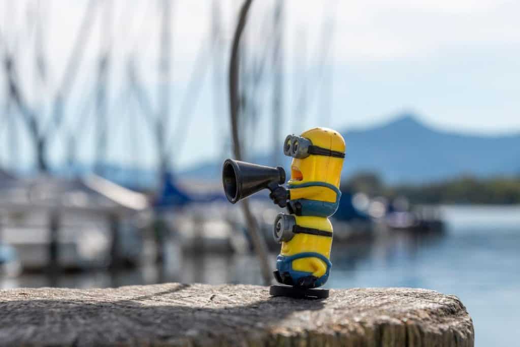 Photo of two minions on top of each other with one holding a microphone by the docks.